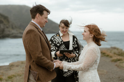 bride and groom stand on the edge of a cliff over the ocean during their Newfoundland elopement ceremony