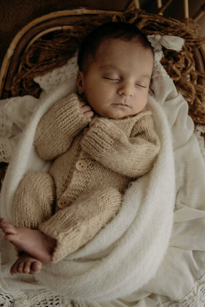 A woman, baby, and young girl are lying on a cozy bed, smiling and cuddling together softly lit by natural light.