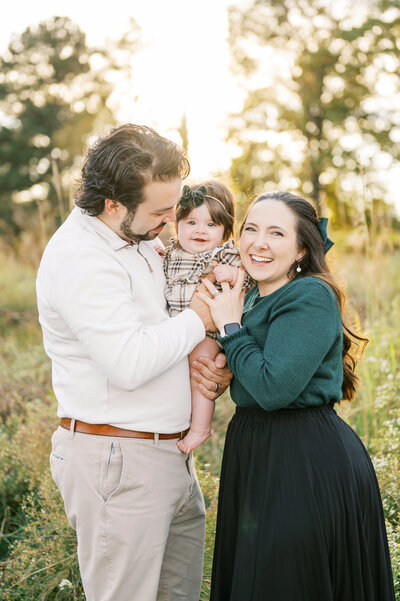 Young parents hold baby girl in tall grassy field during Fall family photo session