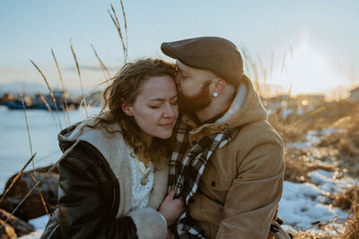 man kissing his fiances cheek at their lake engagement session in Alaska