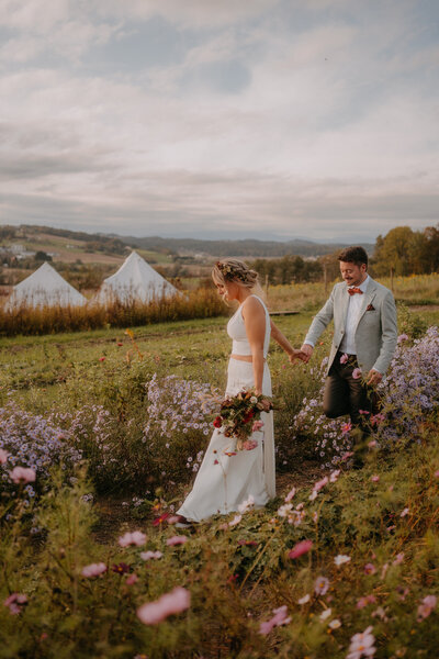 Brautpaar spaziert Hand in Hand durch ein Blumenfeld bei der Hochzeitslocation Vom Hügel in der Steiermark.