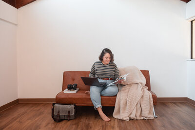 woman sitting on a couch in an empty room working on a laptop