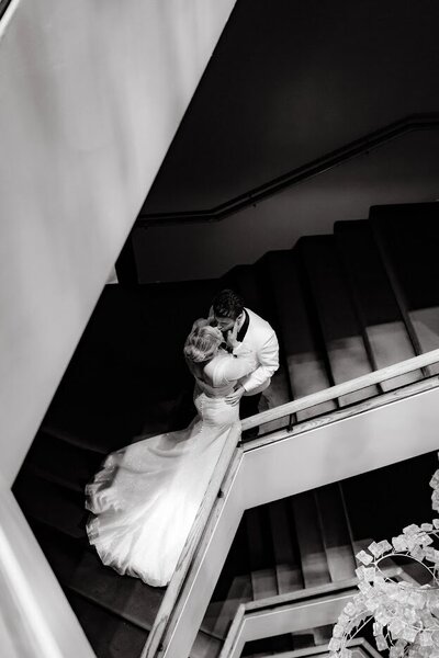 A unique perspective of newlyweds standing on the stairway at the National Arts Centre, viewed from above looking down at the geometrical walls and stairwell.