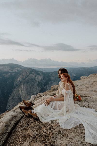 bride and groom sitting on rocky overlook watching the sunset