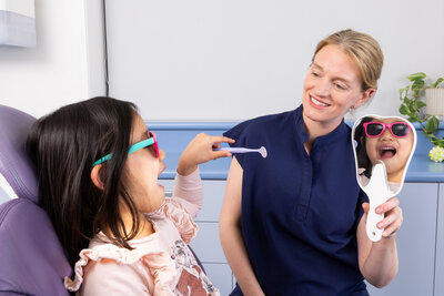 Dentist helping children to feel at ease, showing her a mirror and fun toothbrushes
