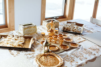 An elegant table setting featuring gold-plated tea sets, ornate trays, and decorative floral favors, arranged on a lace tablecloth. The setup reflects a luxurious and traditional celebration ambiance.