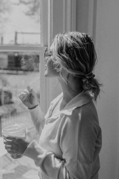 Wedding photographer, Rebekah Soto, standing looking out window while holding coffee