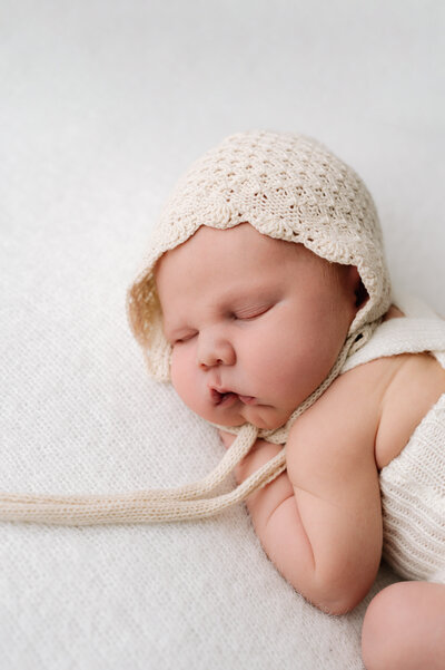 A newborn baby boy sleeping on a white fluffy blanket at a newborn photoshoot in Billingshurst