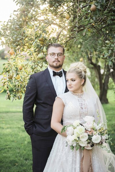 Bride and groom pose under a pear tree on their wedding day