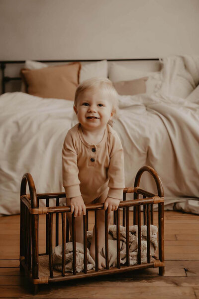 A happy 1 year old boy standing in a wooden crib smiling and looking at the camera