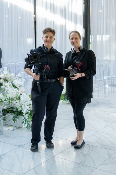 Two videographers smiling with their cameras 