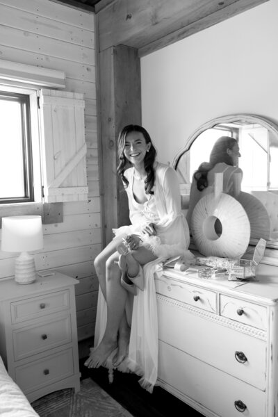 Bride getting ready in a cozy, rustic bridal suite with natural wood accents and a vintage dresser at Bear Ridge Destination.


