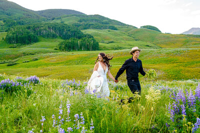 Bride and groom running through a field of Colorado wildflowers with mountain views during their Crested Butte elopement.
