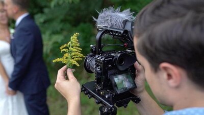 Brian Johnson, owner of With This Ring Wedding Films + Photo, filming a bride and groom during a destination wedding in Mexico under palm trees on a sunny beach