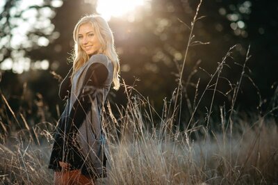 Young woman  standing in a tall grassy area at sunset at Discovery Park in Seattle.