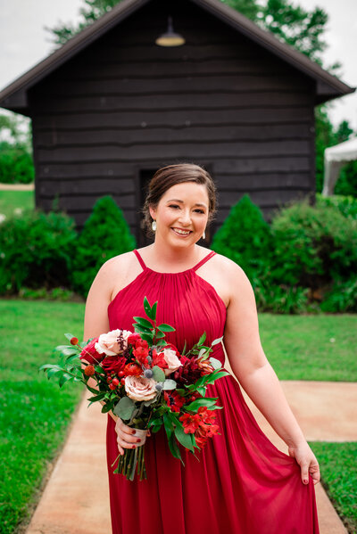 Native American brunette bridesmaid in a bright red dress holding a red and peach bouquet of flowers and berries