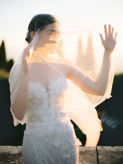 A bride and groom share a kiss at a beautifully set outdoor wedding reception in a French Chateau, captured by International wedding photographer Andreas K. Georgiou. The table is elegantly arranged with floral centerpieces and lit candles. A chandelier hangs overhead, and greenery decorates the venue, embodying luxury wedding photography.