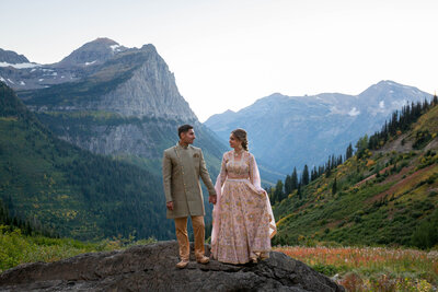 A bride and groom stand on a large rock holding hands and looking at each other after their elopement in Glacier.