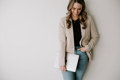 Studio portrait of website copywriter Erika Fitzgerald wearing a tan blazer and holding a laptop, where to works on copywriting services 