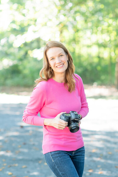 photographer holding a camera wearing a pink sweater