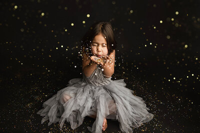 Beautiful girl blowing glitter on black background