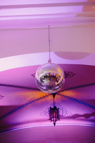 A disco ball hangs from the ceiling surrounded by purple and red lighting