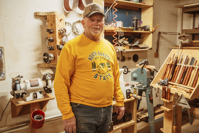 man wearing a yellow shirt, standing in his workshop.