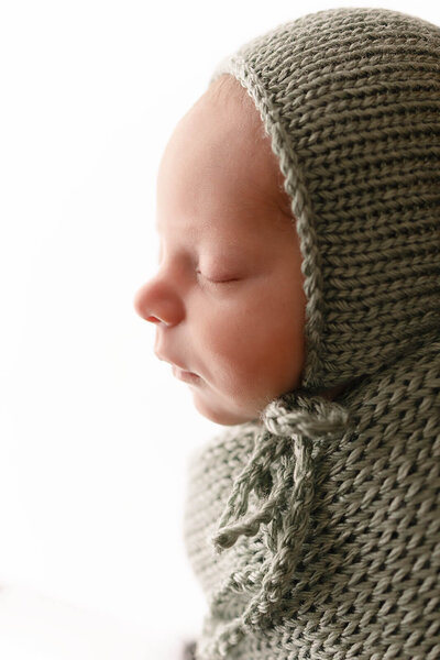 Baby boy wearing green bonnet and green wrap that are knitted sleeping and backlit