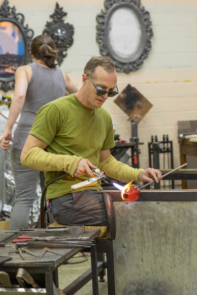 man using torch to heat hand blown glass