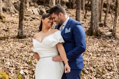 bride and groom sit under a weeping willow tree at Mountain Willow Manor on a white picnic table, the bride has thrown her legs over the grooms lap, exposing her bare feet, they both have their arms around each other as they look into each others eyes. Photo by Chattanooga Wedding Photographer L.Morgan Photography