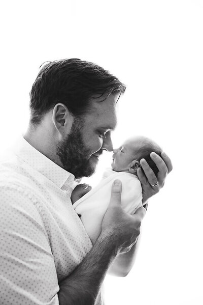 New dad holds his baby nose to nose in a white photo studio.