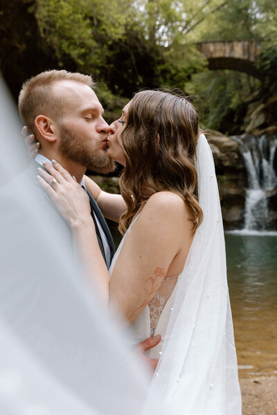 Bride and groom embracing and kissing with the veil held out.