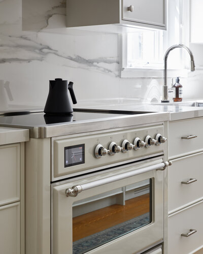 An elegant white stove surrounded by modern white cabinetry and a luxurious marble backsplash