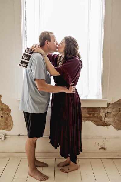 a husband and wife embrace with a sonogram of their new baby from IVF fertility treatments