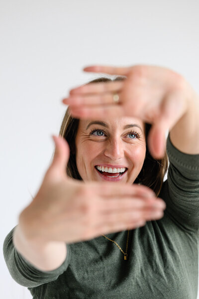 a Denver brand photographer taking a photo of a chiropractor who is holding her hands in front of her face during her Denver Brand photo session.