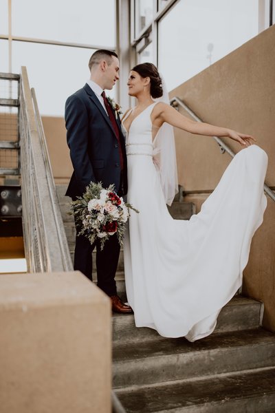 Bride and groom facing each other and looking at one another. Groom is holding flowers for bride. Bride is dropping dress behind her.