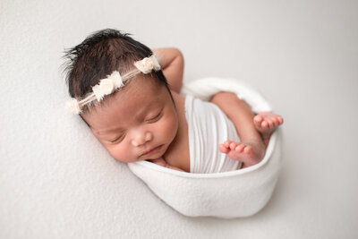 newborn girl wrapped in white fabric with a cream color headband