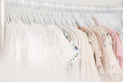 A row of beautiful light colored dresses hanging on a rack in front of a window