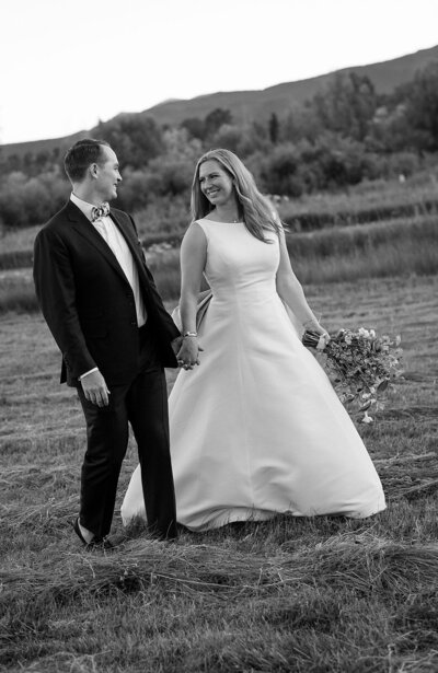 bride and groom walk together in a field in Colorado after wedding