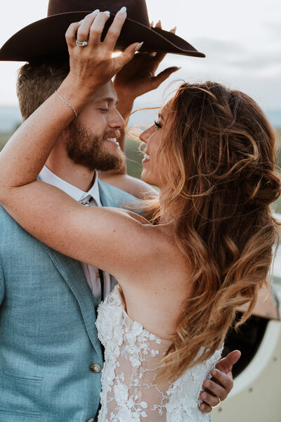 Bride places cowboy hat on groom in golden hour shot by Breckenridge wedding photographer and videographer team.