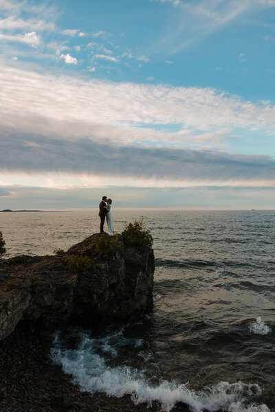 bride and groom standing together with a waterfall in the background and green trees
