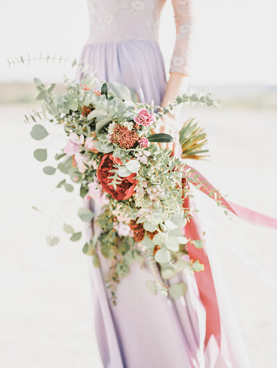 Bridesmaid in purple gown holds the bride's bouquet during photos.