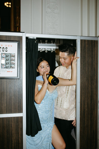 A bride and groom drink champagne on their wedding day while standing in photo booth in San Francisco