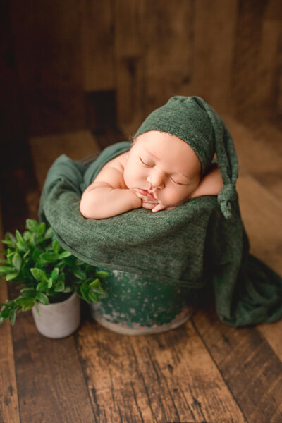 baby boy posed in bucket with green hat, newborn photography ontario