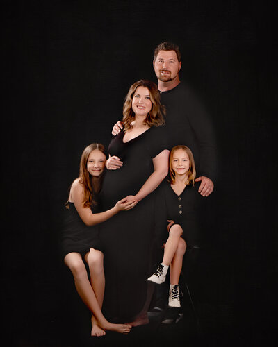 Sophisticated family studio portrait featuring parents and two daughters dressed in black, set against a timeless dark backdrop. Captured in Overland Park, Kansas, this classic setup is ideal for families seeking polished and professional family photography in the Kansas City metro area.