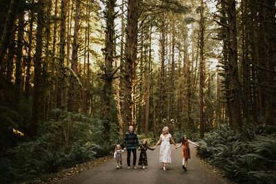 Family walking down a forest road in Ecola State Park with towering trees on either side during their elopement day.