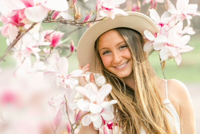 High school senior girl holding her white hat in front of magnolia blossoms