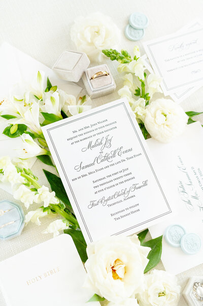 Flowers and wedding invitation sit on mat.