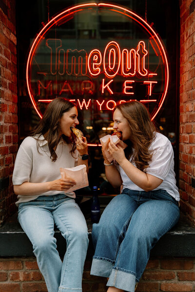 LGBTQ+ couple sharing pastries outdoors in front of a New York City pastry shop during their engagement photoshoot