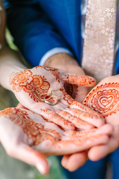 close-up image of hands painted in traditional indian wedding style holdig wedding rings.